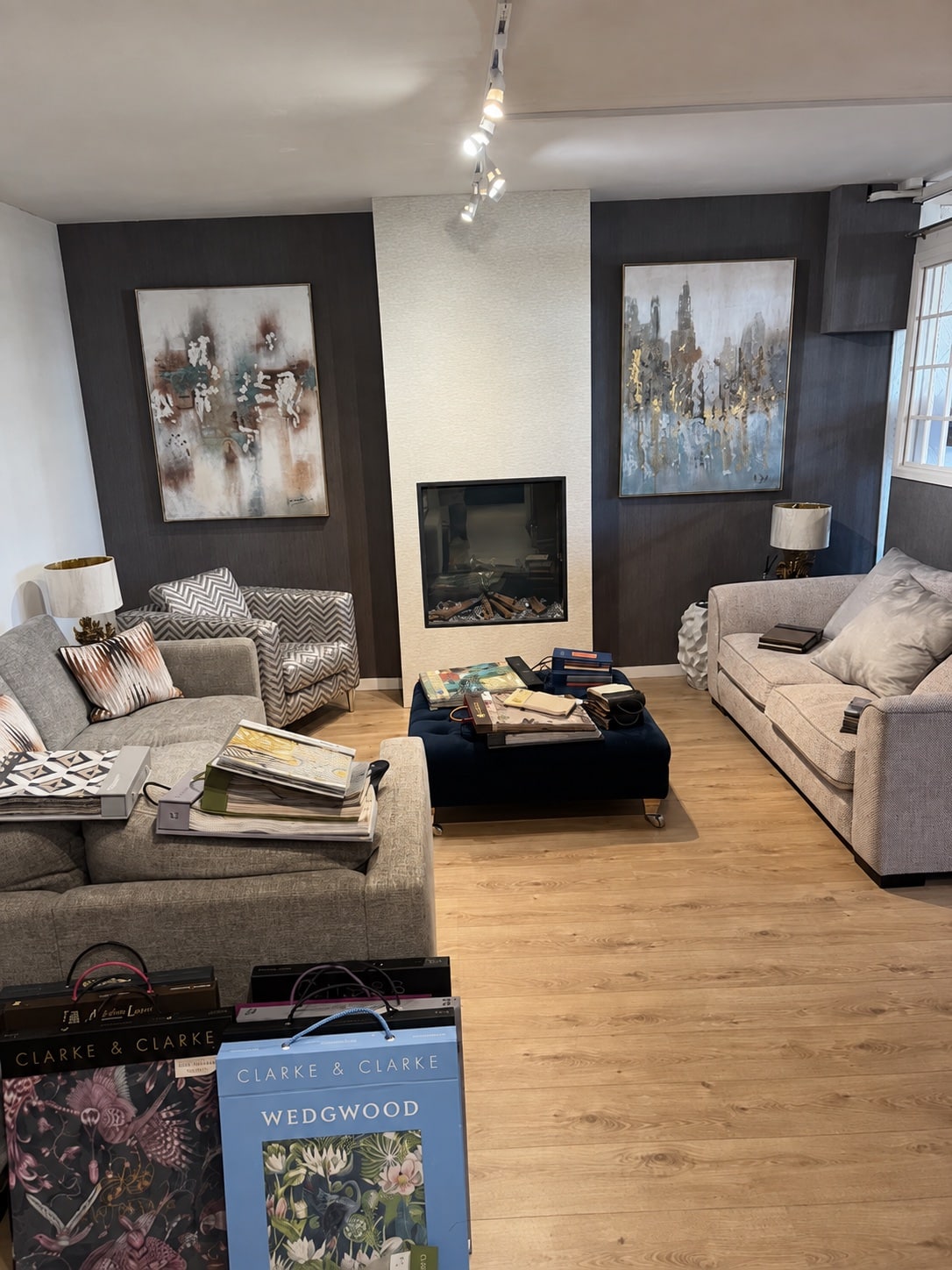 Sofarooms Exeter showroom with upholstered sofas, a patterned armchair, footstools and fabric sample books