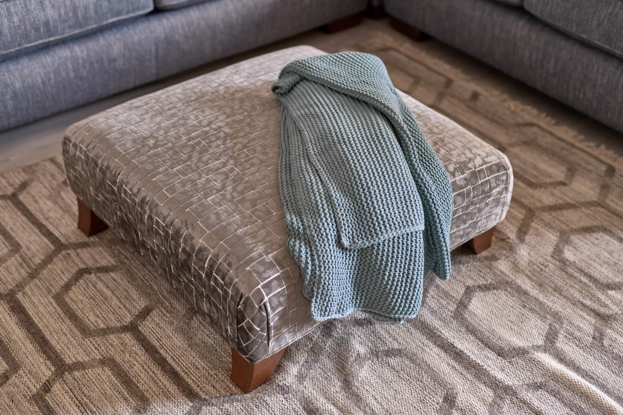 Oddicum patterned footstool with wooden feet and a blue knitted throw.