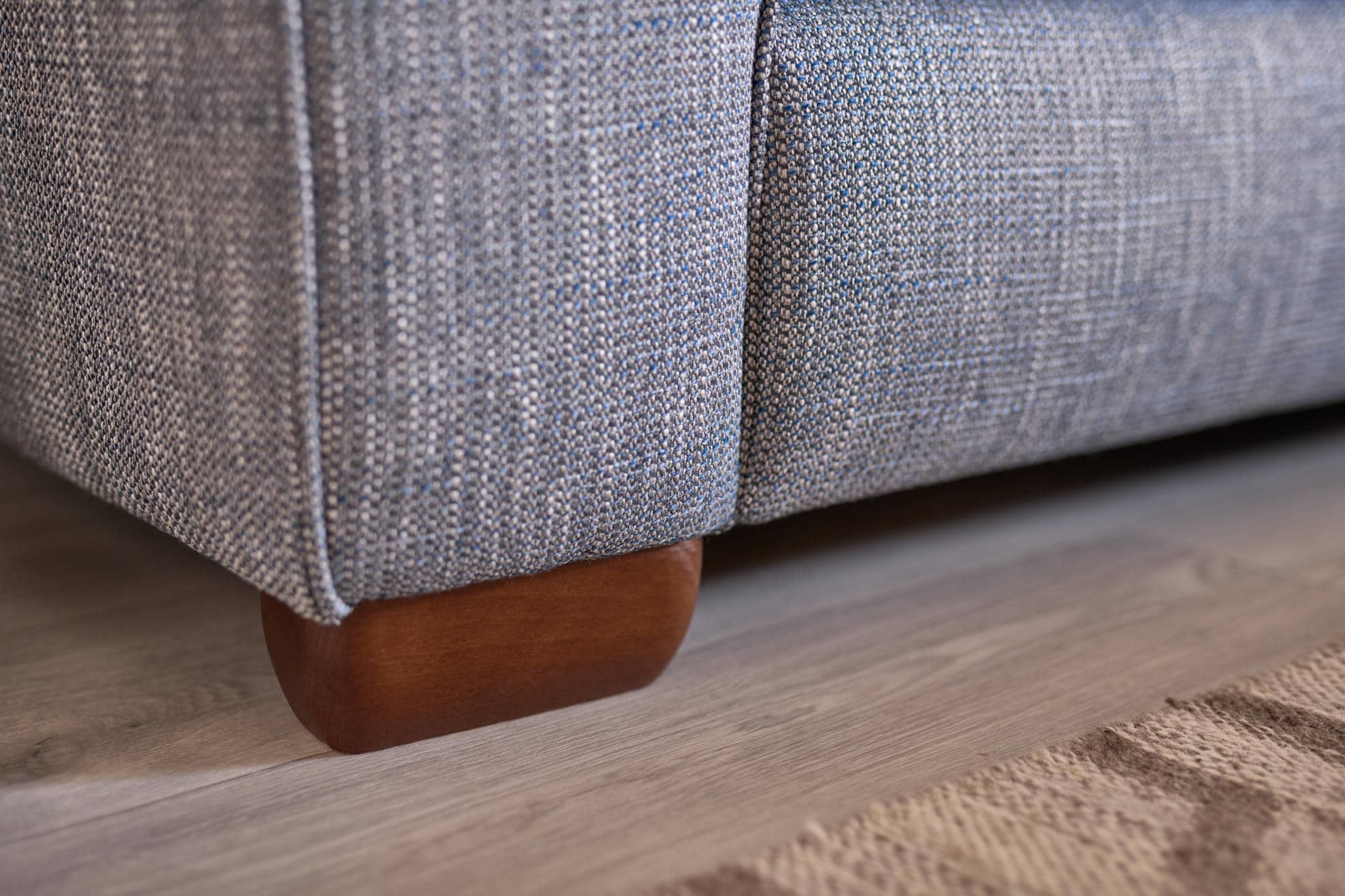 Close-up of the Oddicum sofa showing blue-grey woven upholstery and a wooden foot.